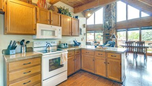 A kitchen with wooden cabinets, a microwave, and a stove. There is a stone pillar and a view of the outdoors through large windows.