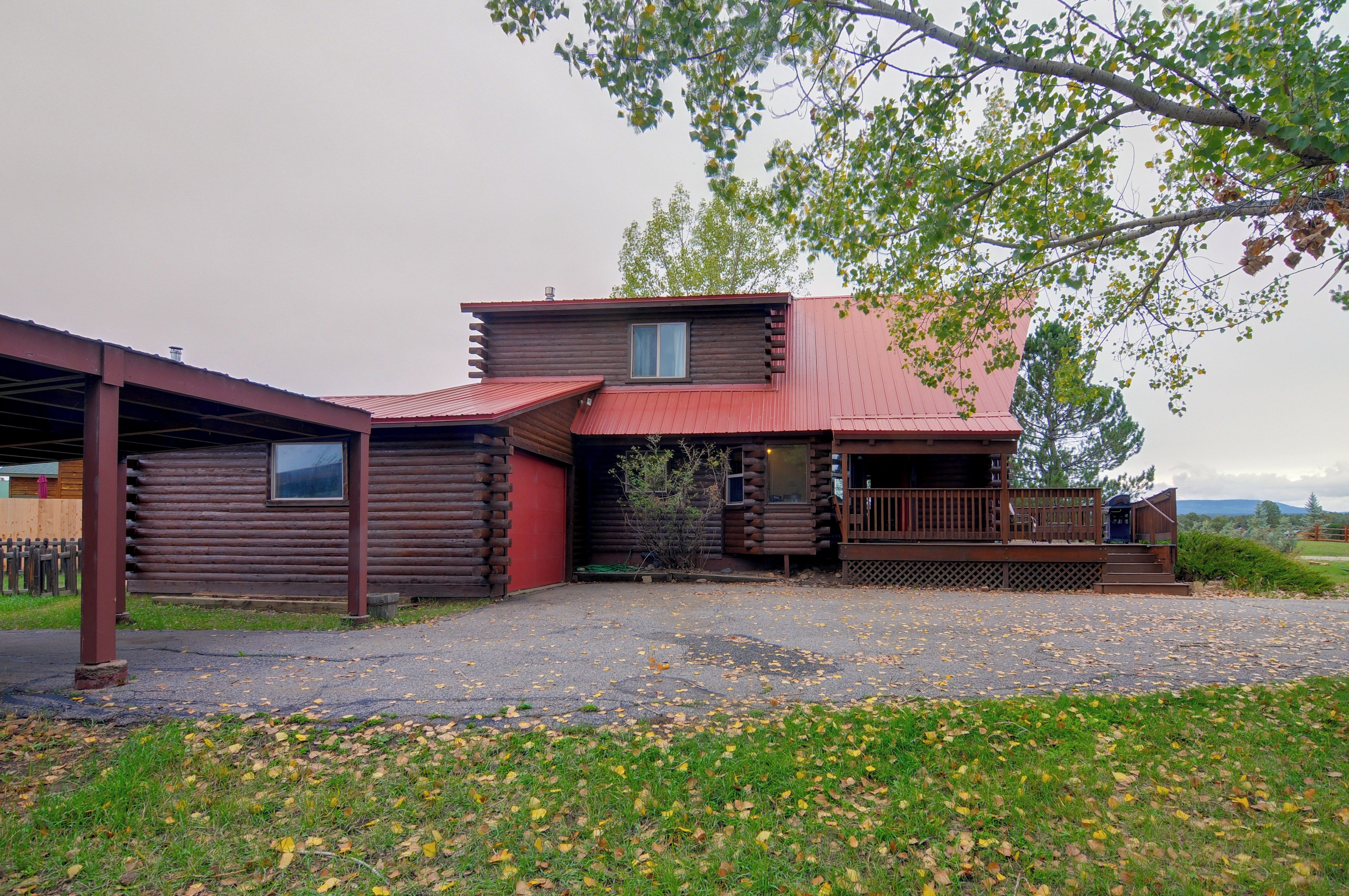 A log cabin with a red roof, a covered porch, and a gravel driveway.