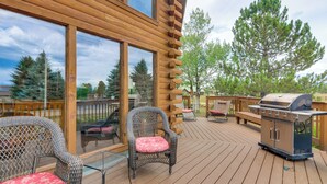 A deck with wicker chairs, a grill, and a view of trees.