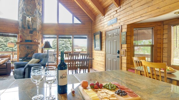 A wooden interior with a stone pillar, a dining table with a cheese board, wine glasses, and a bottle.