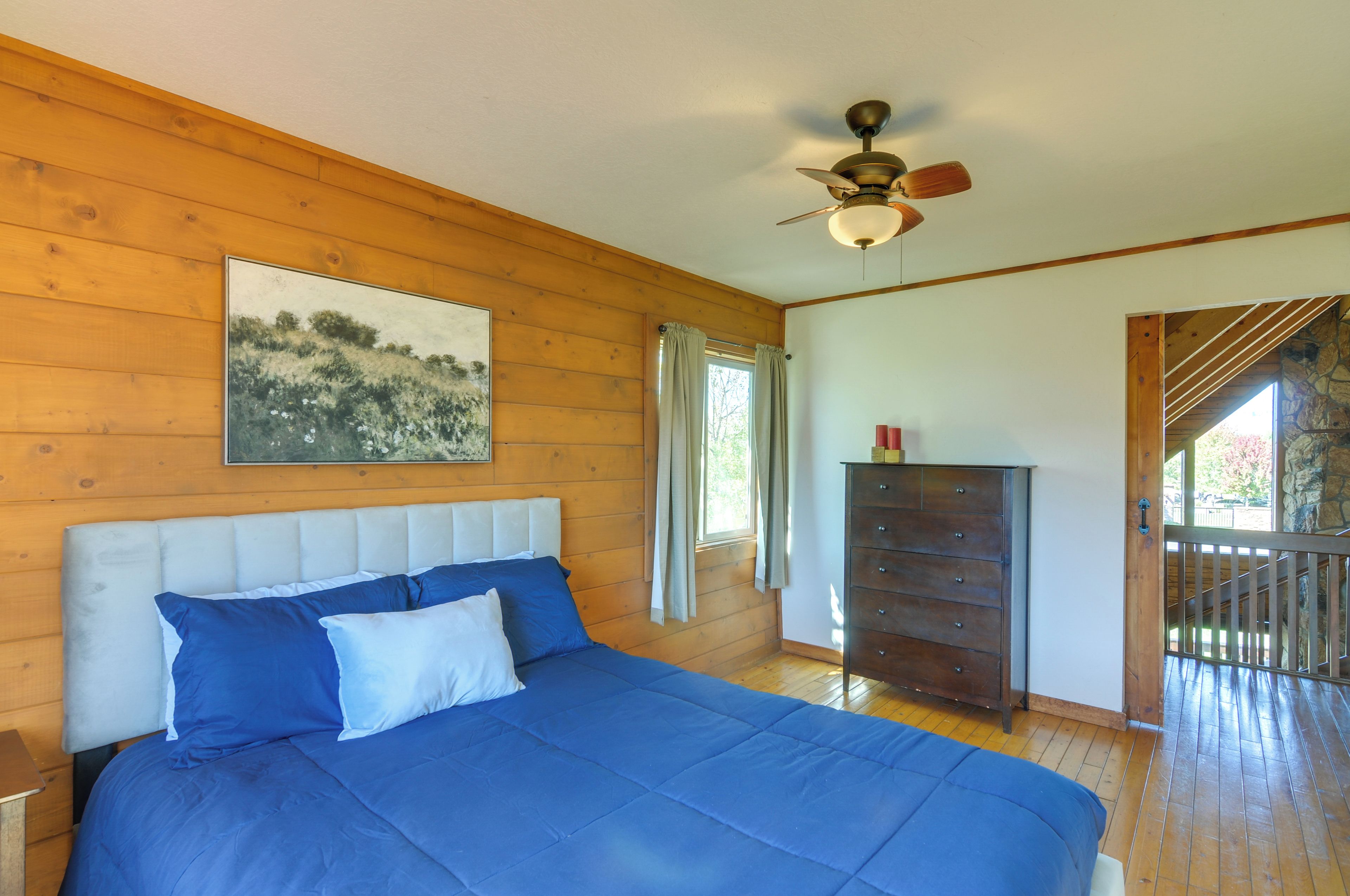 Une chambre à coucher avec un lit, une commode, un ventilateur de plafond et un tableau accroché au mur.