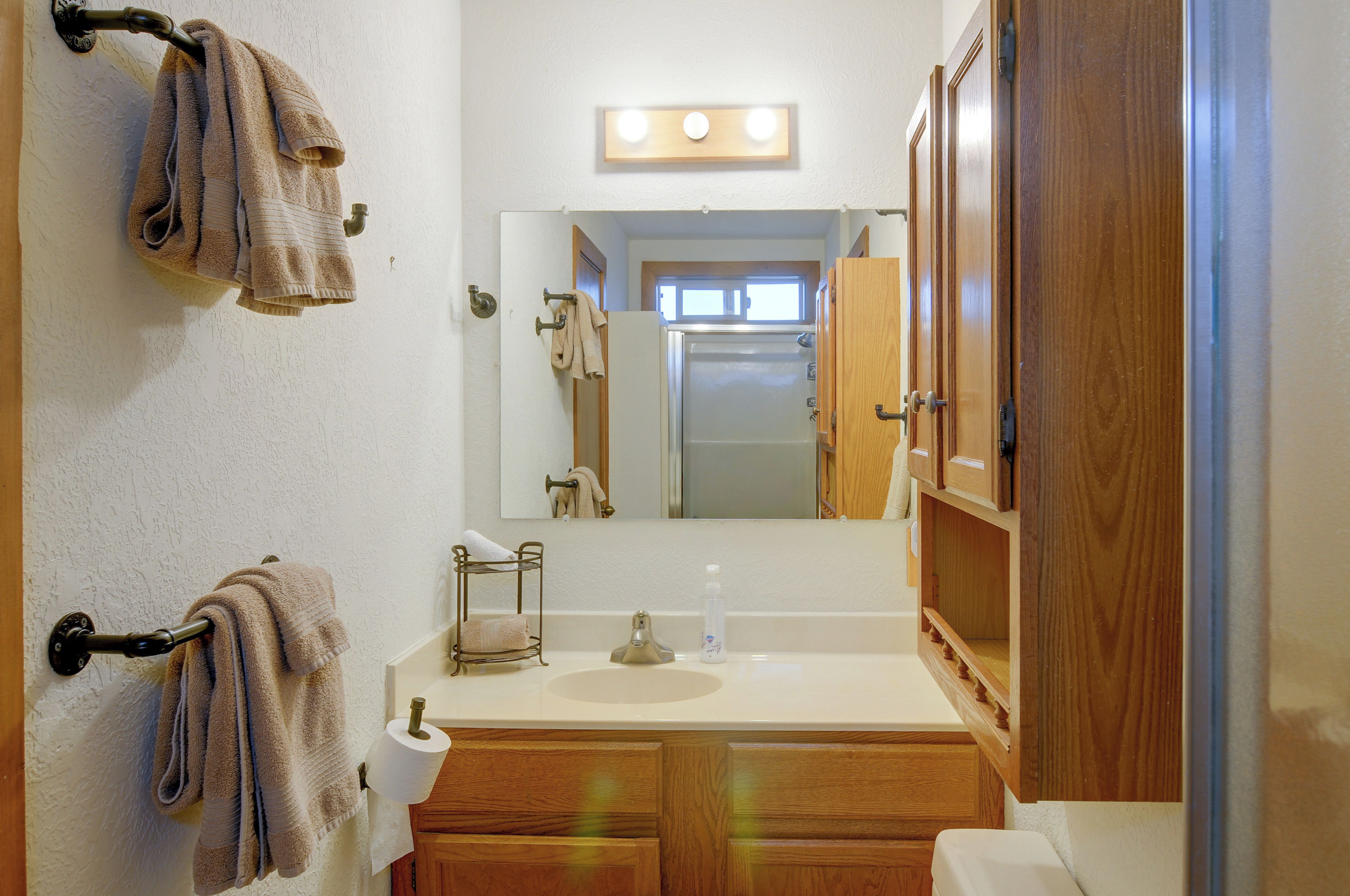 A bathroom with a toilet, sink, mirror, towel rack, and a wooden cabinet.