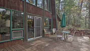 Guests can enjoy the cabin's expansive deck with seating and large windows offering a view of the surrounding forest.