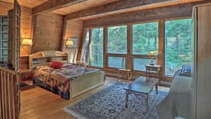 Ein gemütliches Blockhaus mit einem großen Bett, einem Holztisch und Blick auf den Wald durch große Fenster.