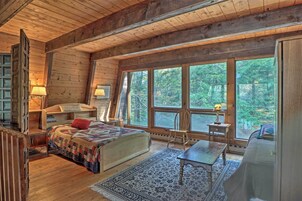 Una cabaña acogedora con una cama grande, un escritorio de madera y vistas al bosque a través de ventanas amplias.