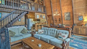 Ein rustikales Blockhaus-Interieur mit einer Holztreppe, einem Essbereich und einem Wohnzimmer, möbliert mit einer Couch und einem Couchtisch.