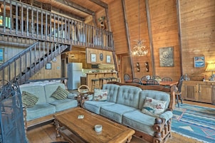A rustic cabin interior with a wooden staircase, a dining area, and a living room furnished with a sofa and coffee table.