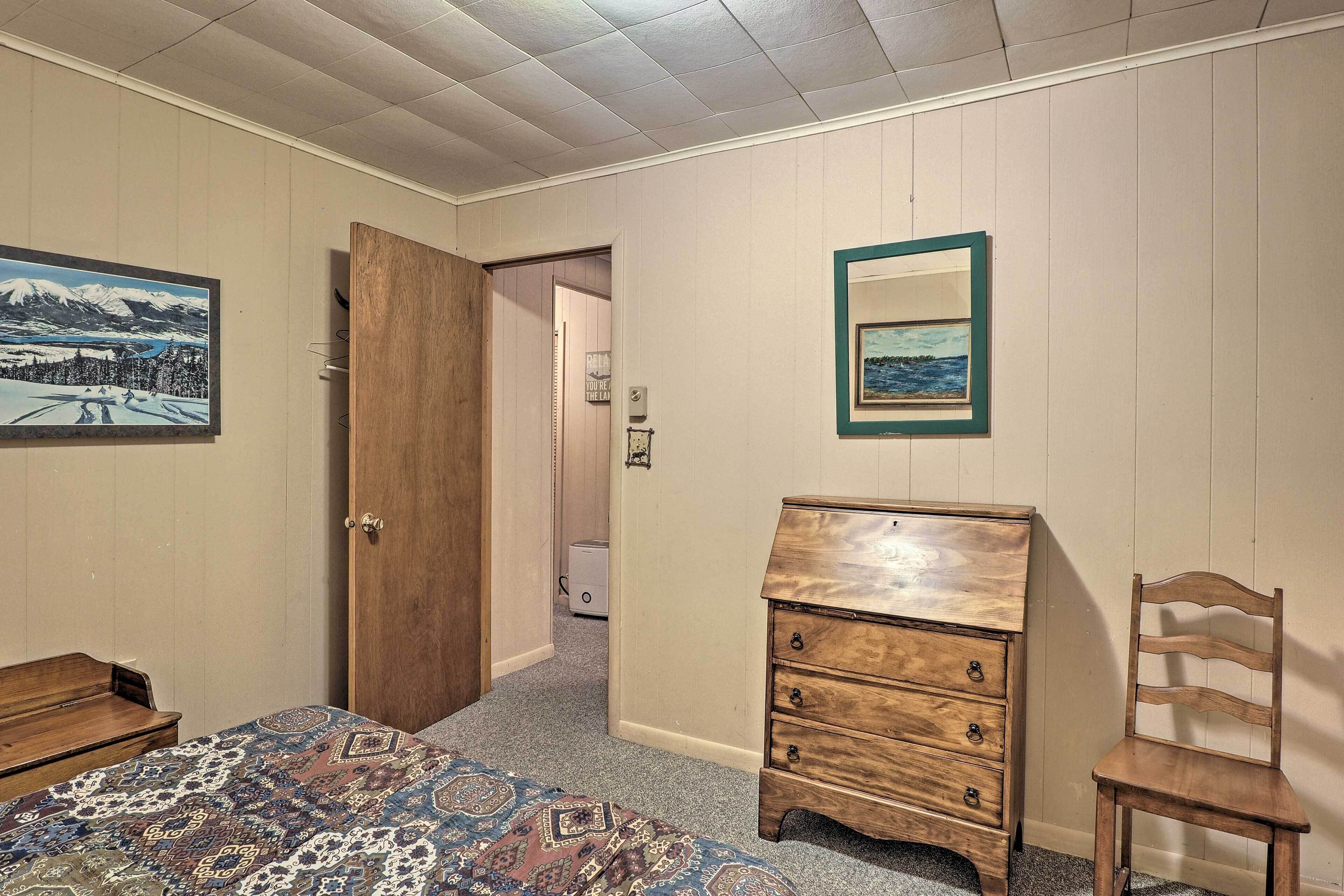 A bedroom with a bed, a wooden dresser, a chair, and two framed pictures on the wall.