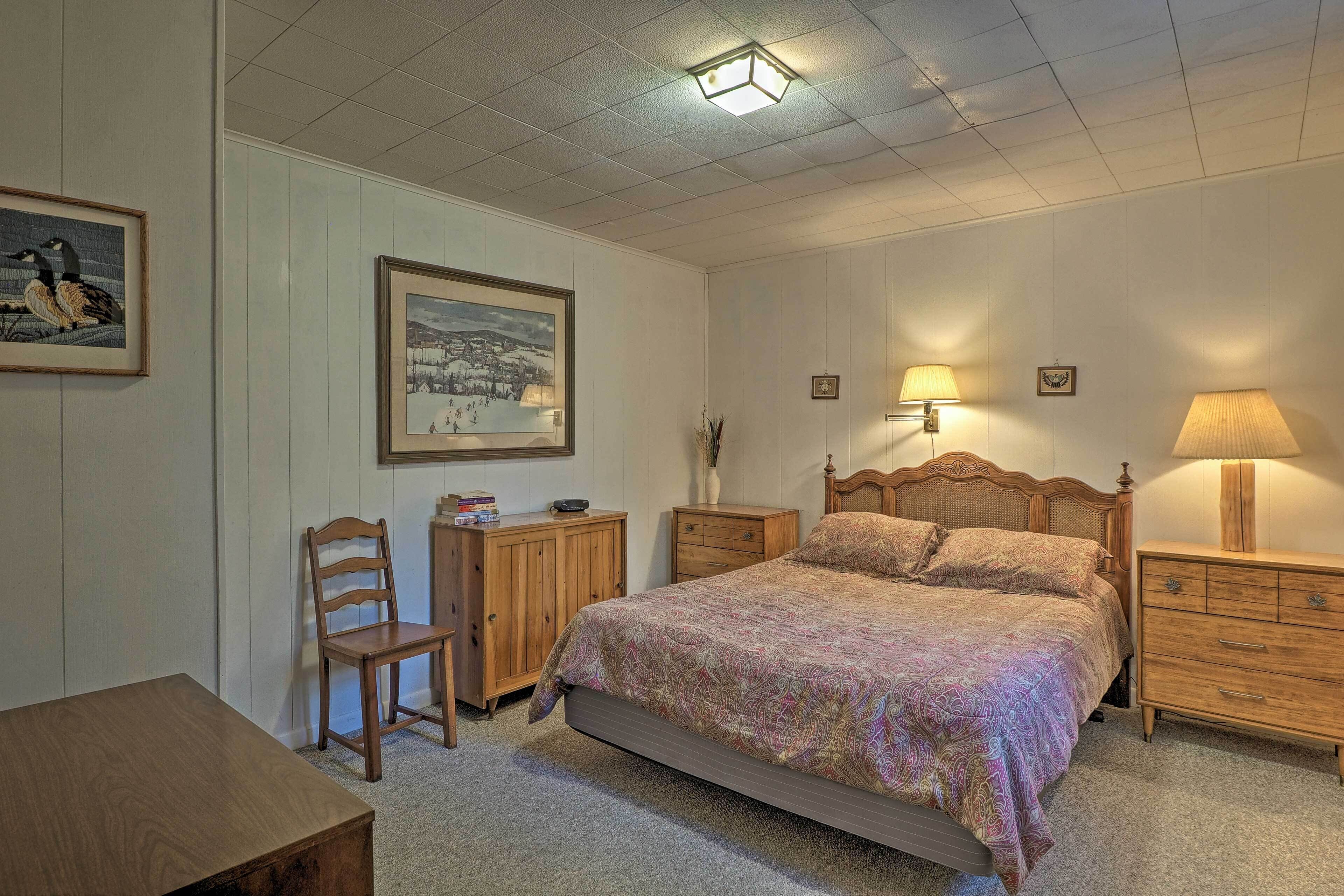 A bedroom with a large bed, two bedside tables, a wooden chair, a desk, and a framed picture on the wall.