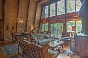 A spacious log cabin interior with a large dining table, multiple seating options, and a wood-burning stove.
