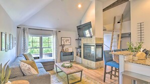 A spacious living room with a sofa, coffee table, and a TV mounted on the wall. A kitchen area with a stove and a ladder is visible. - 5 Mi to Ski Resort: Breck Penthouse Studio (Breckenridge)