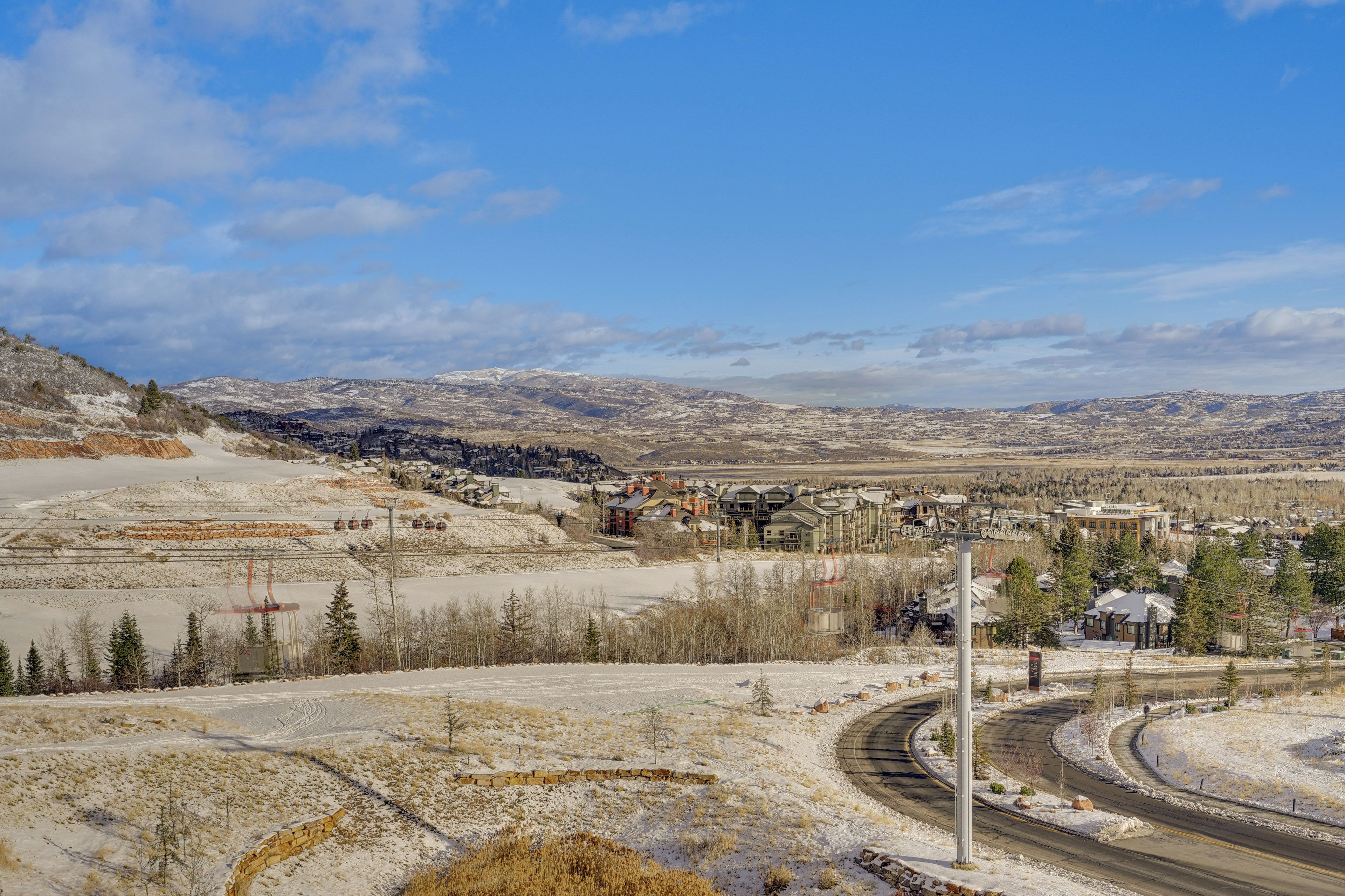 A snow-covered landscape with a winding road, buildings, and distant mountains.