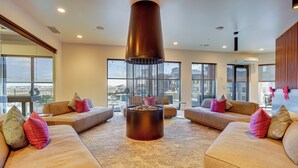 A modern living room with a central fire feature, large windows, and comfortable seating.