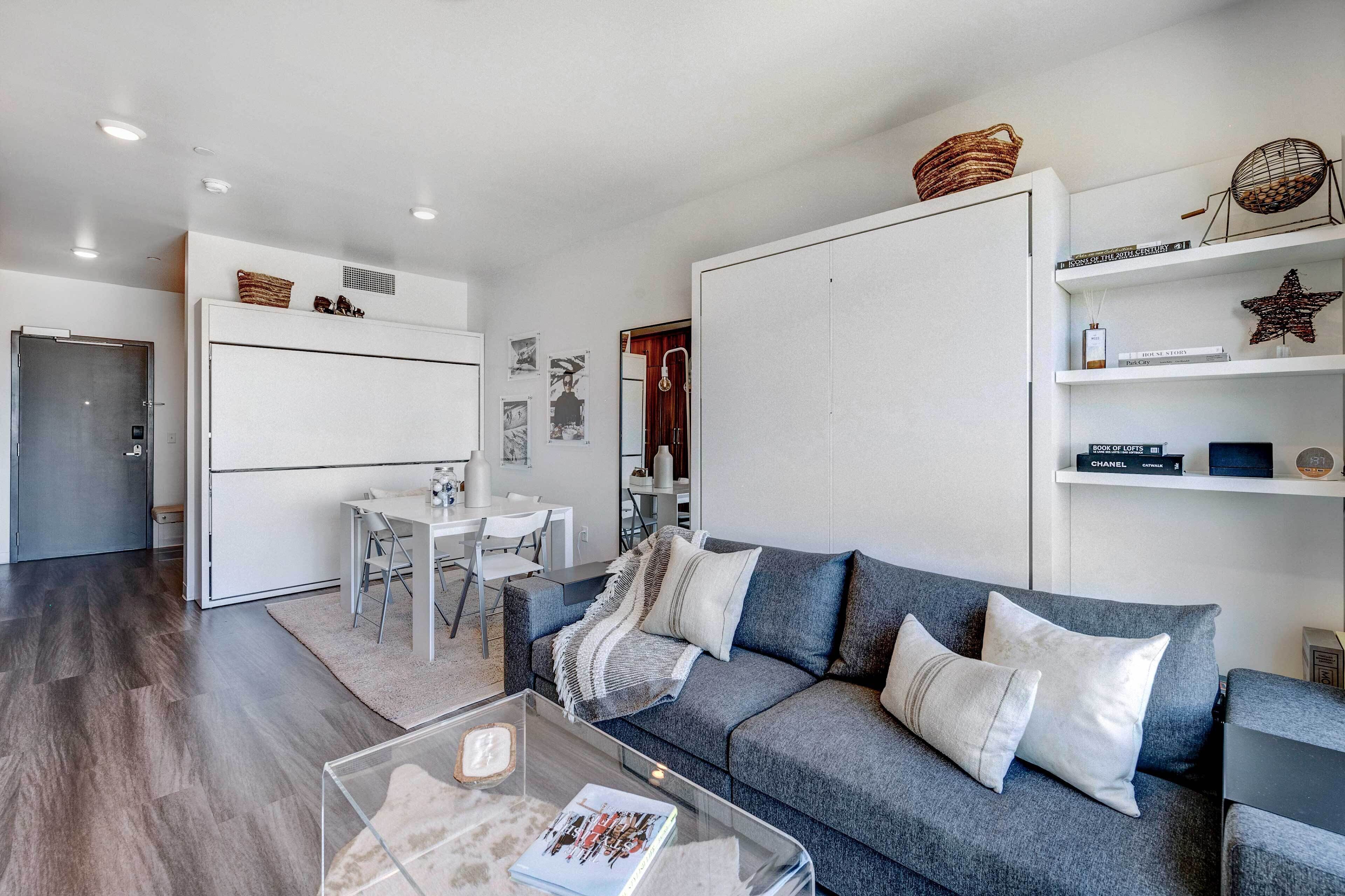 A modern living room with a grey sofa, a glass coffee table, and a dining area with a white table and chairs.