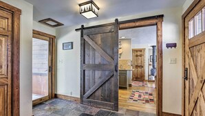 A rustic interior with a large wooden sliding barn door, a stone-tiled floor, and a kitchen area visible through the door. - Spacious Grand Lake Cabin w/ Hot Tub & Deck (Grand Lake)