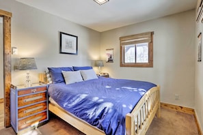 A bedroom with a wooden bed, a dresser with drawers, two bedside lamps, a framed picture on the wall, and a window with a wooden blind. - Spacious Grand Lake Cabin w/ Hot Tub & Deck (Grand Lake)