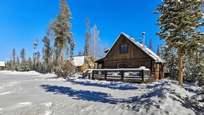 A wooden cabin with a snow-covered roof, surrounded by snow-laden trees and a clear blue sky. - Spacious Grand Lake Cabin w/ Hot Tub & Deck (Grand Lake)