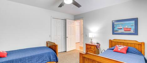 Un dormitorio con dos camas de madera, un ventilador de techo y una puerta que da a otra habitación.