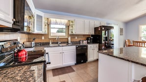 A modern kitchen with white cabinets, granite countertops, a red kettle, and a dishwasher. - Watts Bar Lake Escape: Private Boat Dock + Ramp! (Spring City)