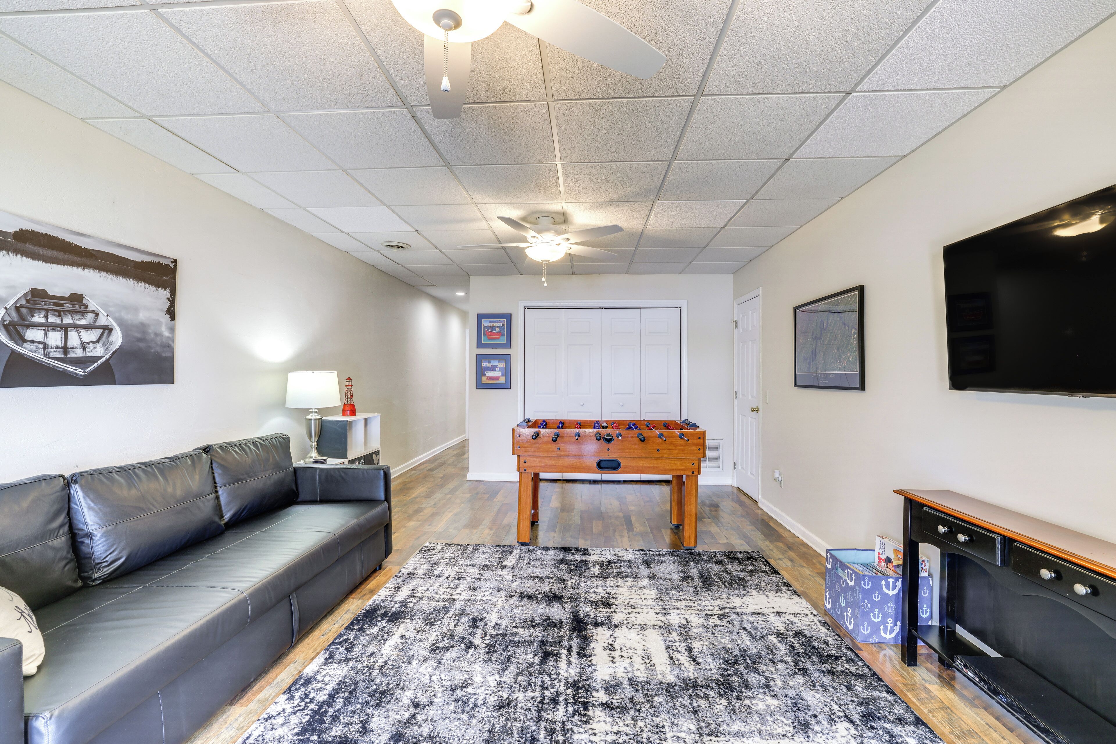 A living room with a sofa, a foosball table, a television, and a ceiling fan.