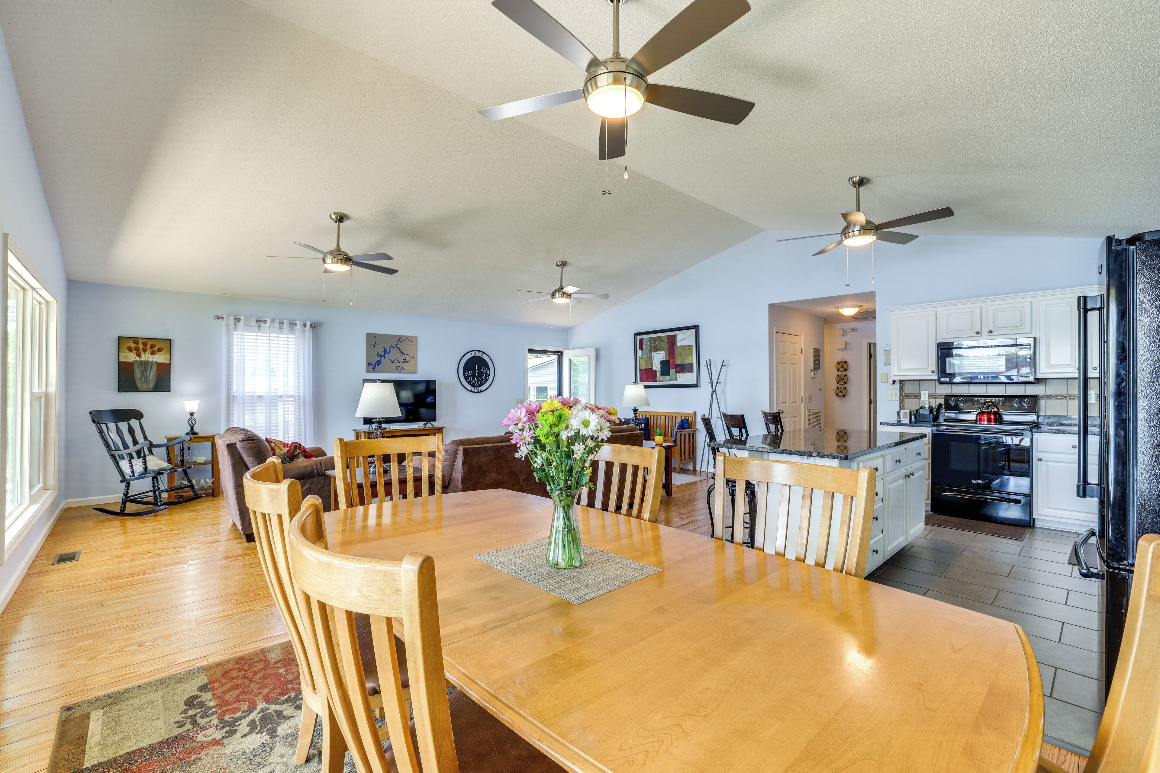 A spacious dining area with a wooden table and chairs, a vase of flowers, and ceiling fans.