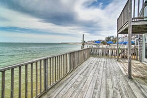 A wooden pier extending into a calm body of water, with a view of a distant shoreline and a building with blue awnings in the background. - Harbor Views + Private Deck: Waterfront P-town Apt (Provincetown)