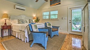 A bedroom with a bed, two blue wicker chairs, a ceiling fan, an air conditioner, a window with blinds, and a door. - Seagrove Beach Studio - 1/4 Mi to Beach Access! (Santa Rosa Beach)