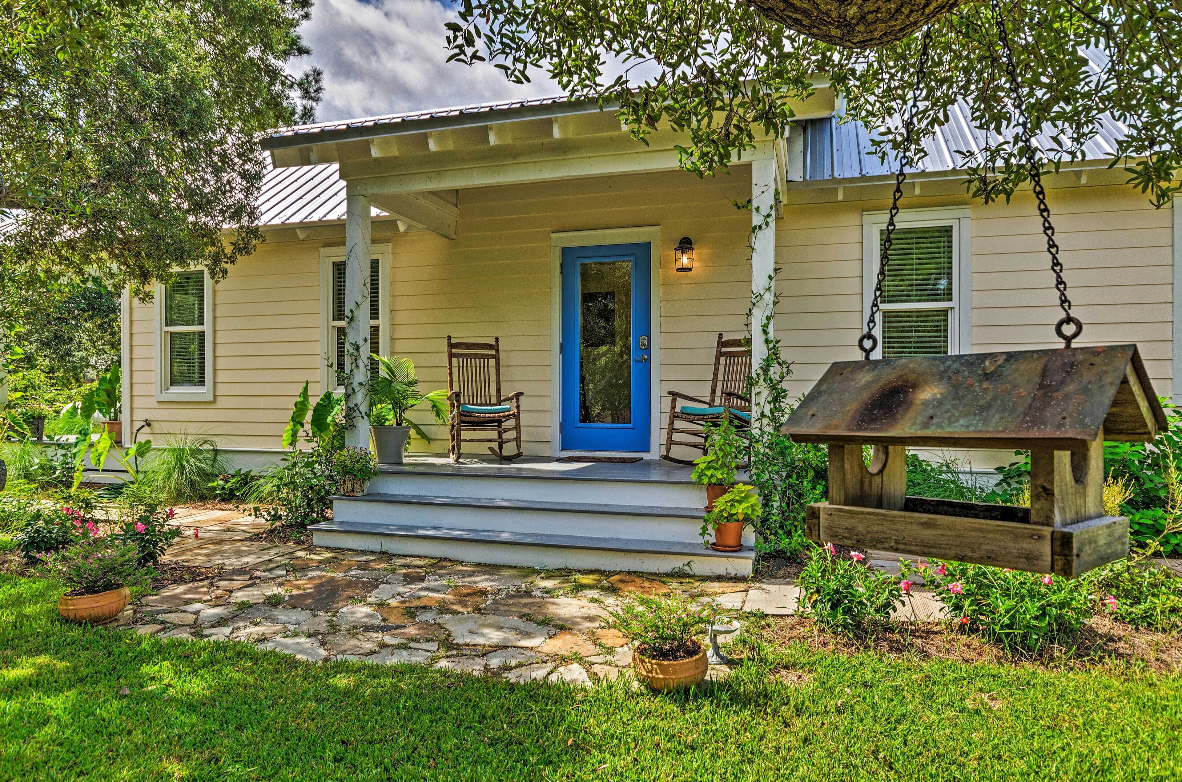 A house with a blue front door, a porch with two rocking chairs, and a hanging bird feeder.
