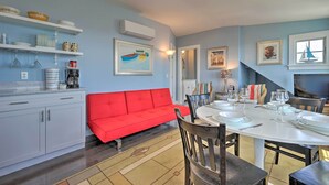 A dining area with a red sofa, white dining table, and chairs. There are shelves with dishes and a painting on the wall. - Couples Retreat! Penthouse Near Commercial Street (Provincetown)