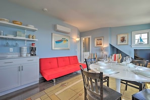 A dining area with a red sofa, white dining table, and chairs. There are shelves with dishes and a painting on the wall. - Couples Retreat! Penthouse Near Commercial Street (Provincetown)