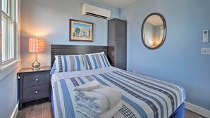 A bedroom with a bed, a nightstand, a lamp, an air conditioner, a wardrobe, a mirror, and a picture on the wall. - Couples Retreat! Penthouse Near Commercial Street (Provincetown)
