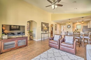 A spacious living room with a large TV, leather sofas, wooden flooring, and a ceiling fan.