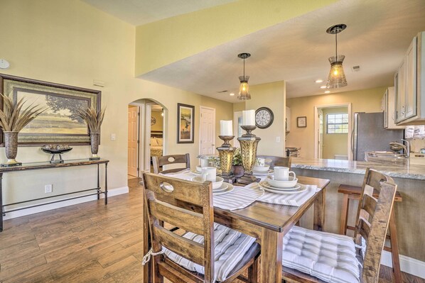 A dining area with a wooden table set for four, surrounded by chairs with cushioned seats. A buffet table with dishes is visible in the background. - 1 Block to Branson Strip: Condo w/ Views & Pool! (Branson)