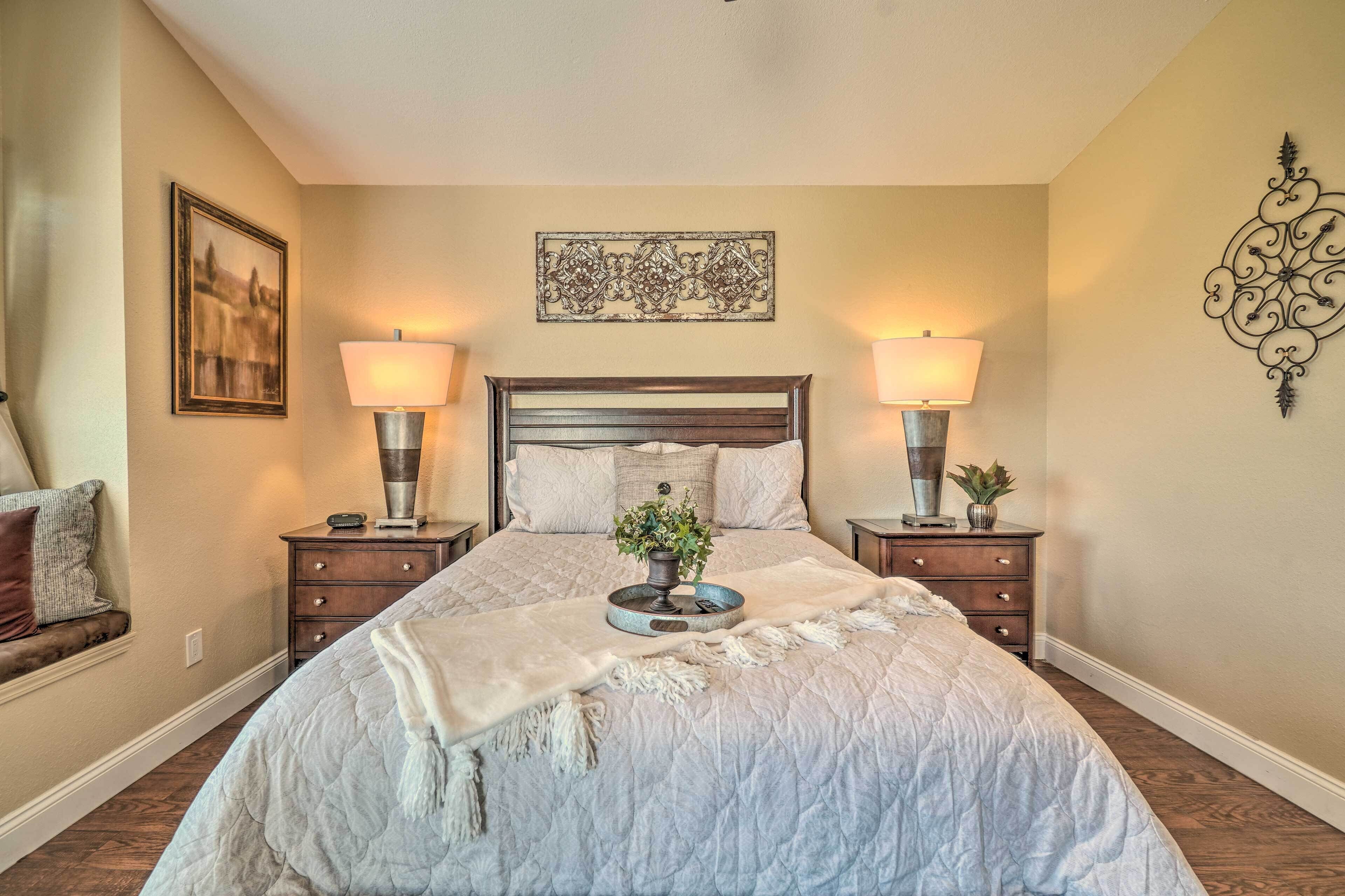 A bedroom with a large bed, two bedside tables with lamps, a decorative wall piece above the bed, and a small plant on the bedside table.