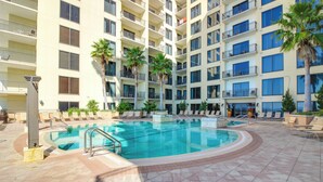 A multi-story hotel with a swimming pool, palm trees, and sun loungers. - Breezy Panama City Beach Condo w/ Private Balcony! (Panama City Beach)