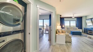 A hotel room with a washer and dryer, a living area with a sofa, a TV, and a balcony with a view. - Breezy Panama City Beach Condo w/ Private Balcony! (Panama City Beach)