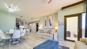 A spacious living area with a dining set, a sofa, and a blue ottoman. - Breezy Panama City Beach Condo w/ Private Balcony! (Panama City Beach)