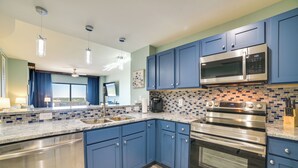 A modern kitchen with blue cabinets, stainless steel appliances, and a tiled backsplash. - Breezy Panama City Beach Condo w/ Private Balcony! (Panama City Beach)