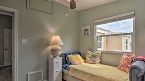 Un dormitorio con cama, mesita de noche, ventana con persianas y ventilador de techo.