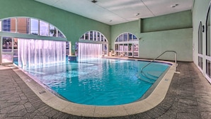 Una piscina interior con agua cristalina, suelo de baldosas y ventanales arqueados.