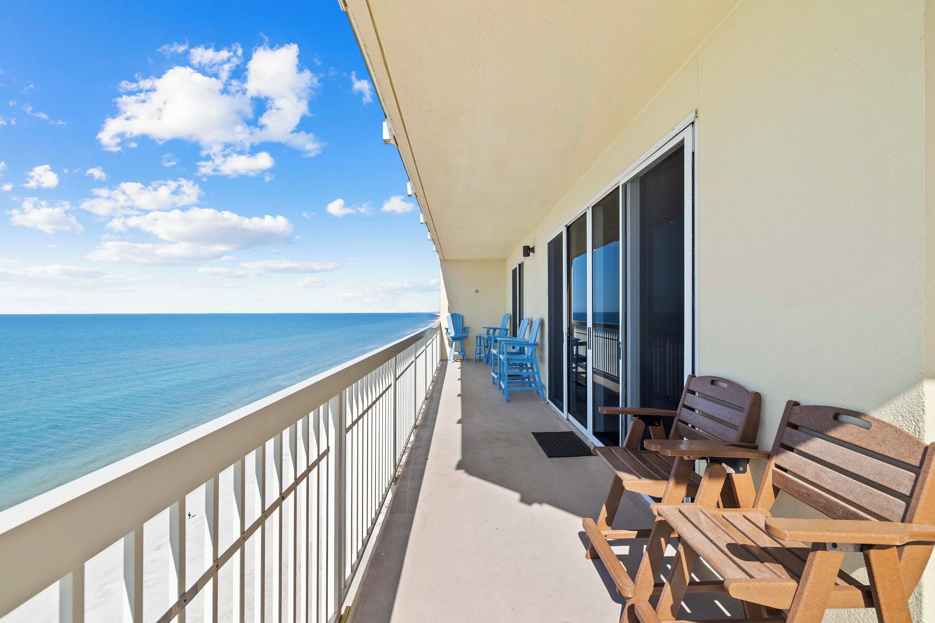 A balcony with a view of the ocean, wooden furniture, and a glass door leading to an interior space.