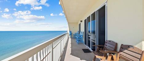 A balcony with a view of the ocean, wooden furniture, and a glass door leading to an interior space.