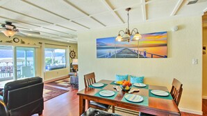 A dining area with a wooden table, chairs, and a bench. There is a painting on the wall, a ceiling fan, and a view of the outdoors through large windows. - Lakefront Retreat w/ Dock, Paddle Boards & Kayaks! (Clearlake)