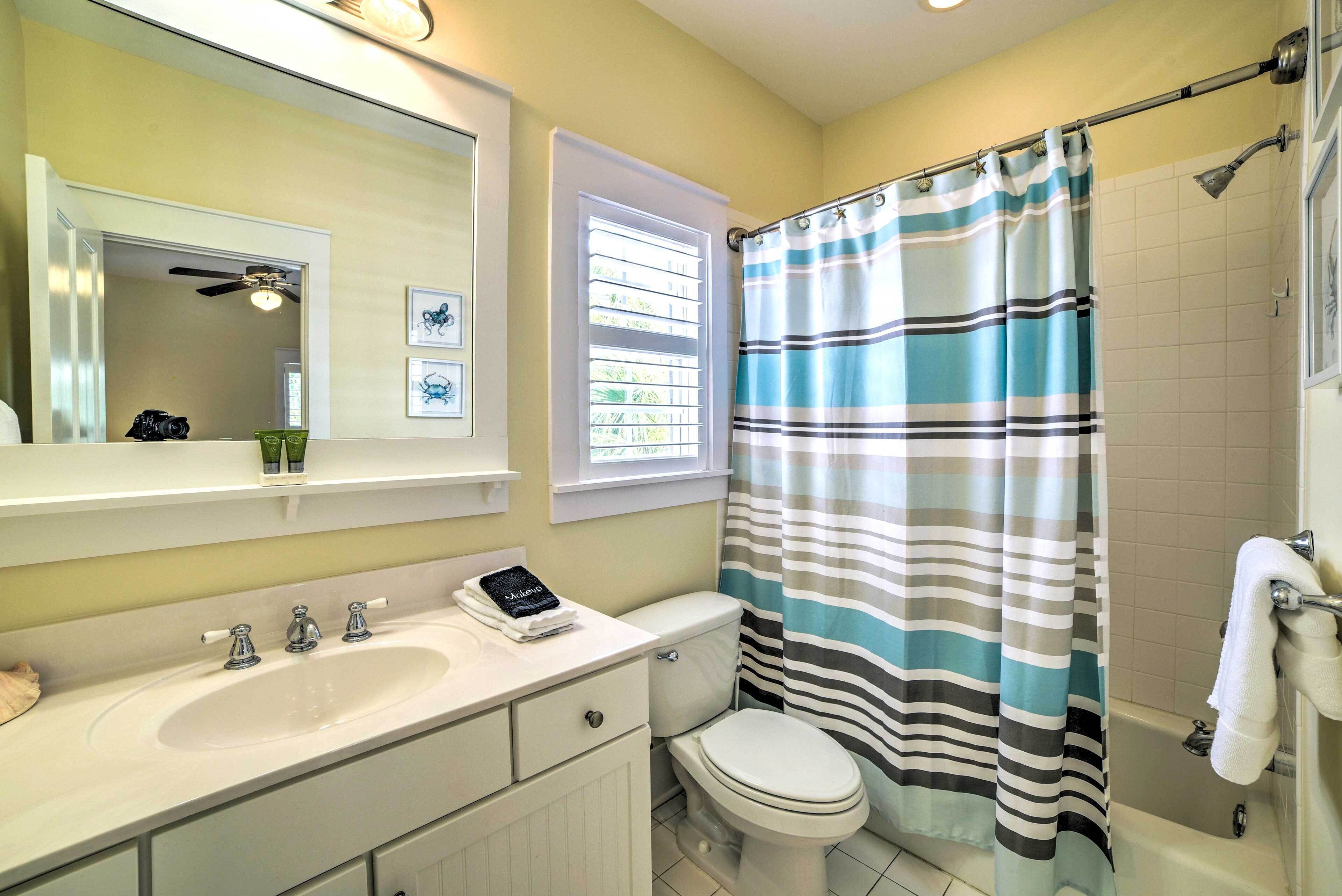 Une salle de bain avec un lavabo blanc, des toilettes, une douche avec un rideau à rayures et un ventilateur de plafond.