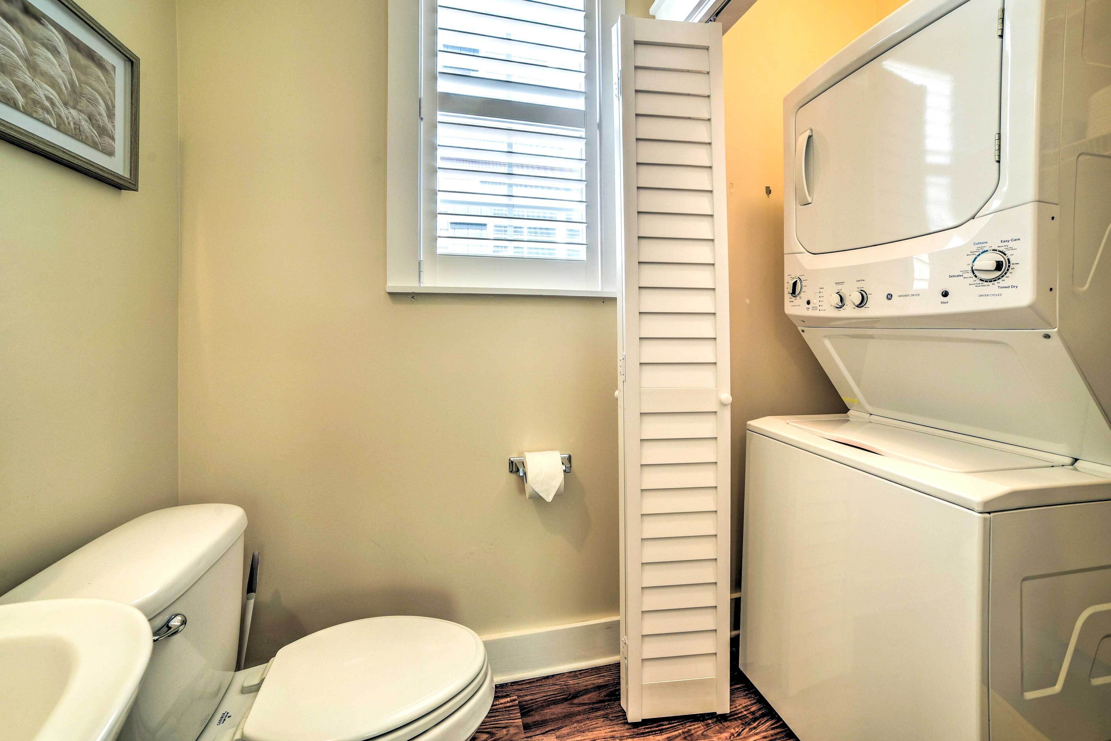 A compact bathroom with a toilet, a window with blinds, and a front-loading washer.
