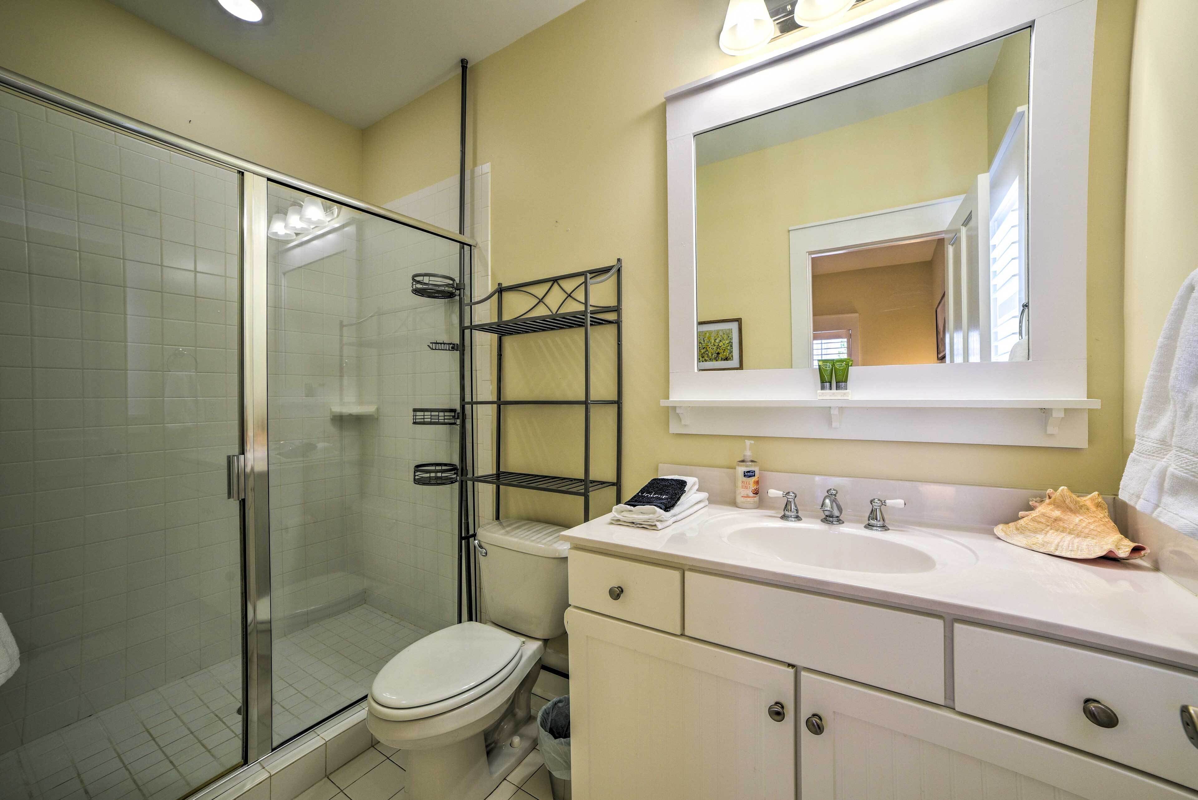 Une salle de bain avec une douche à parois de verre, des toilettes, un lavabo avec un miroir au-dessus et une étagère contenant des articles de toilette.