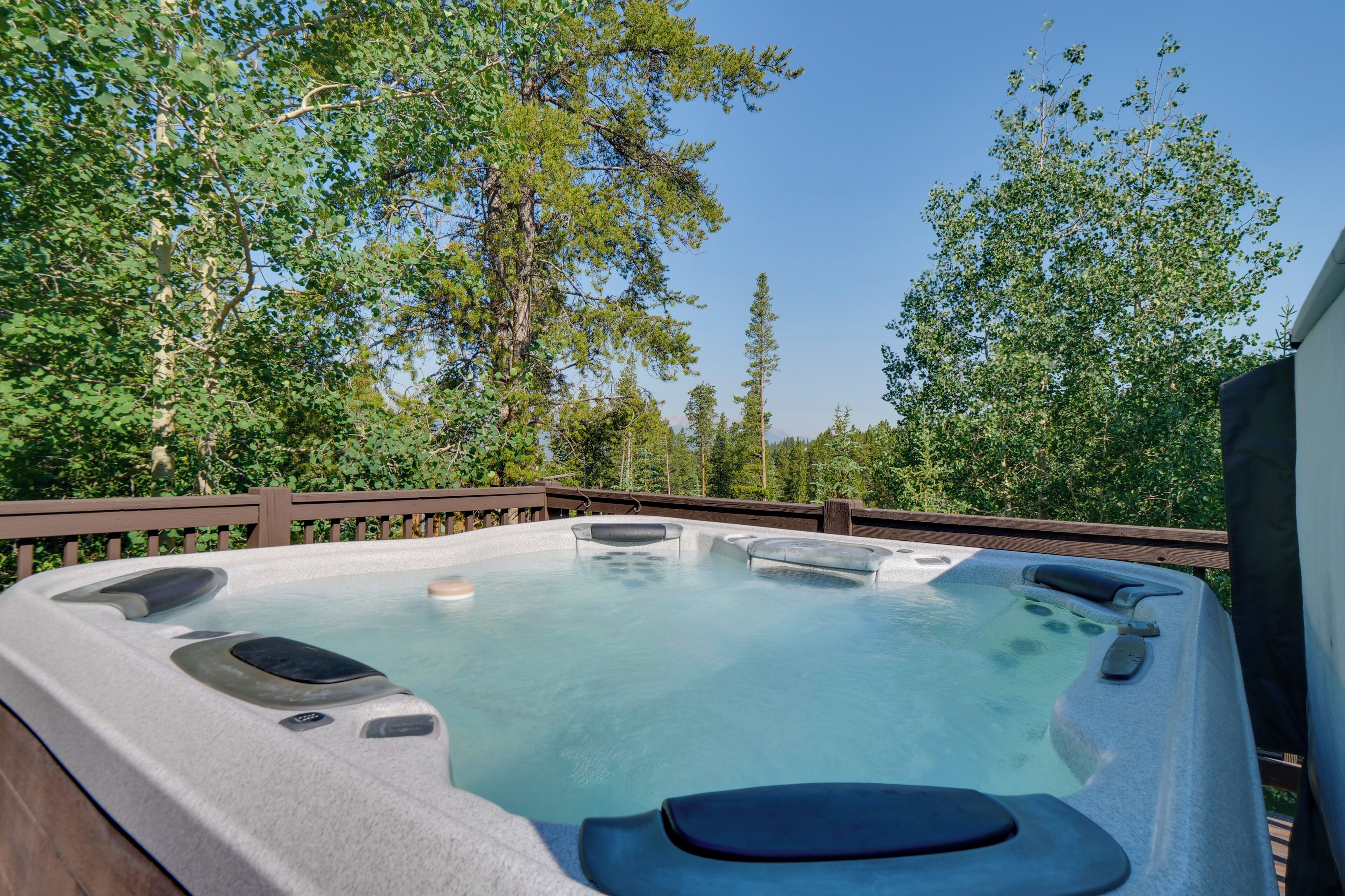 A hot tub surrounded by a wooden deck with trees in the background.