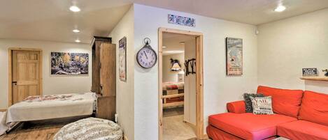 A cozy room with a bed, a red sofa, a wooden door, and a wall clock.