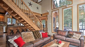 Un espacio habitable amplio con una escalera de madera, sofás de cuero y un ventanal con vistas al exterior.