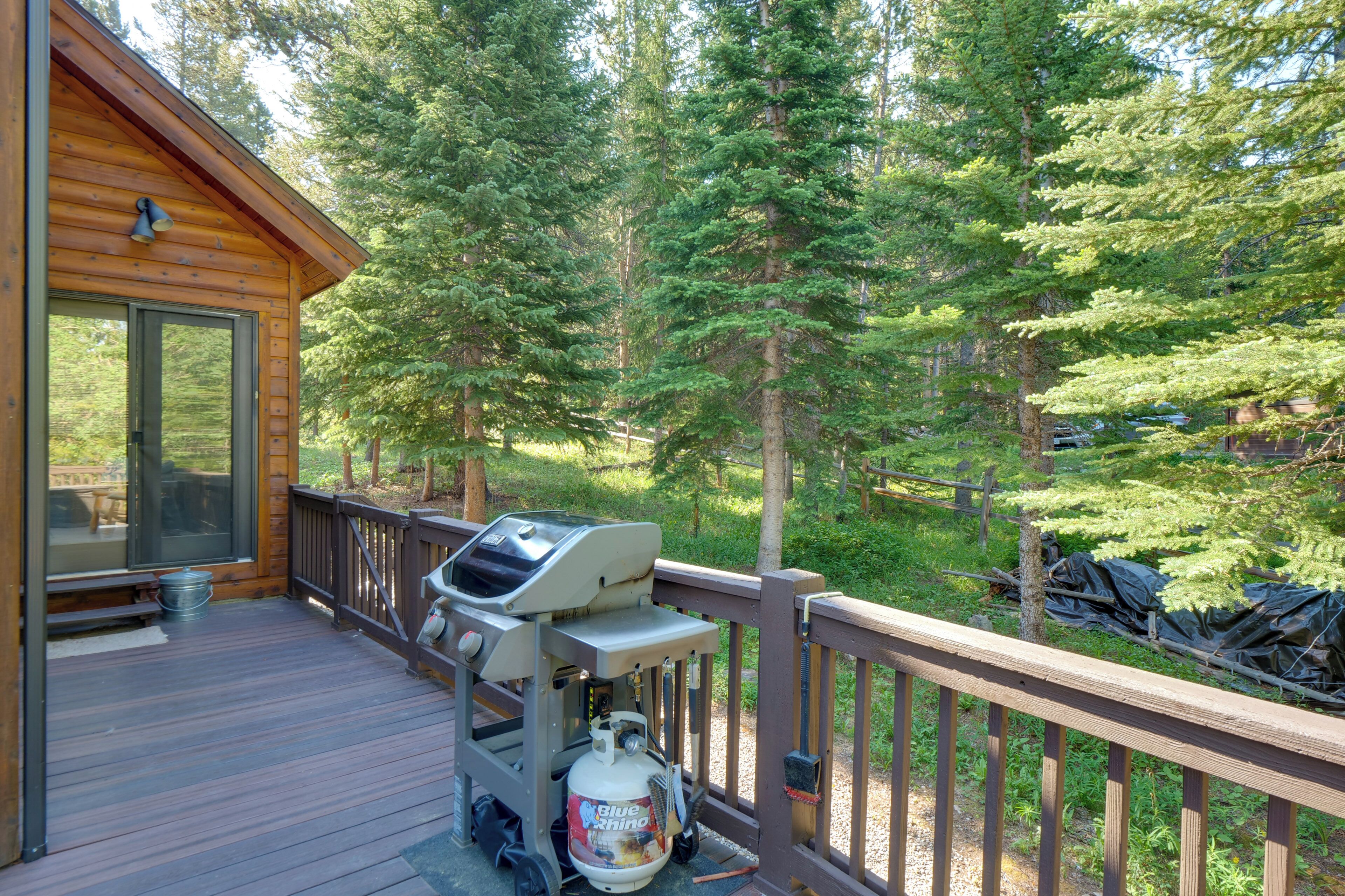 A wooden deck with a grill and propane tank, surrounded by trees.